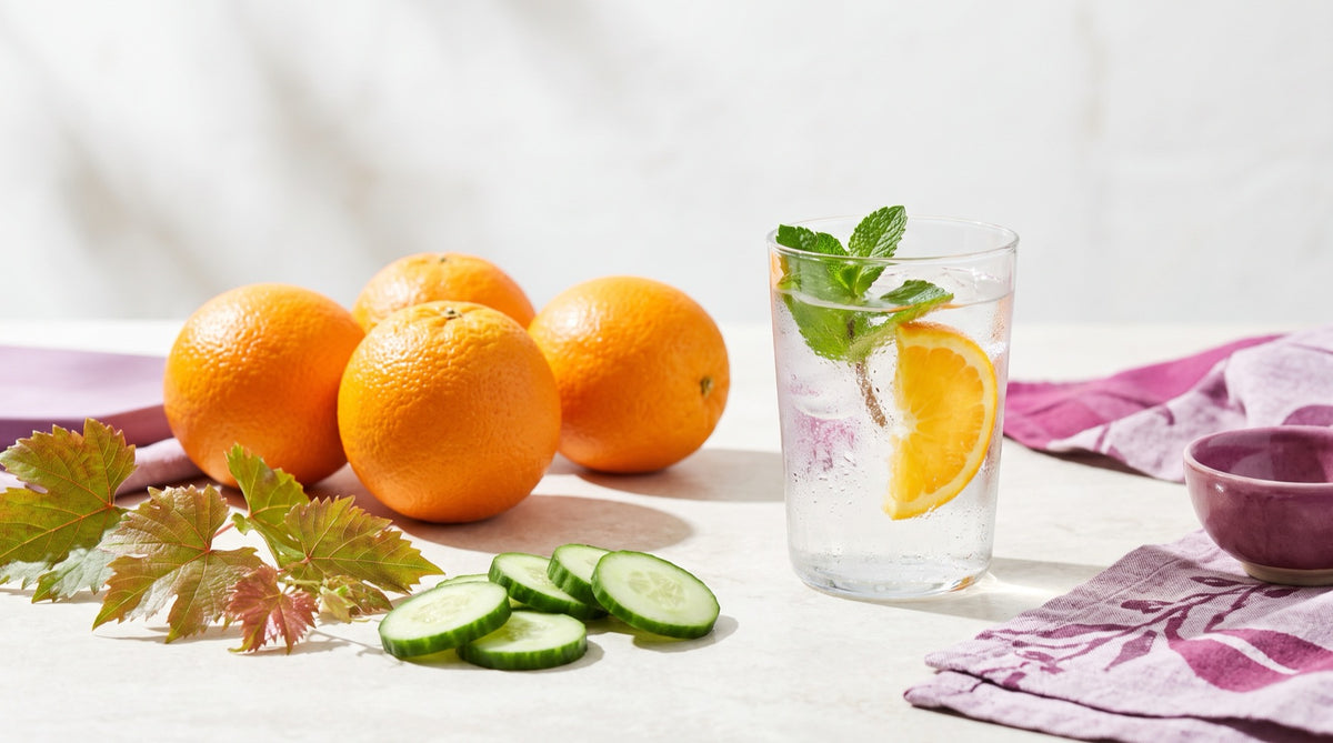Bicchiere di acqua fresca con menta e arancia, arance, cetriolo e foglie di vite rossa: freschezza per le gambe d'estate