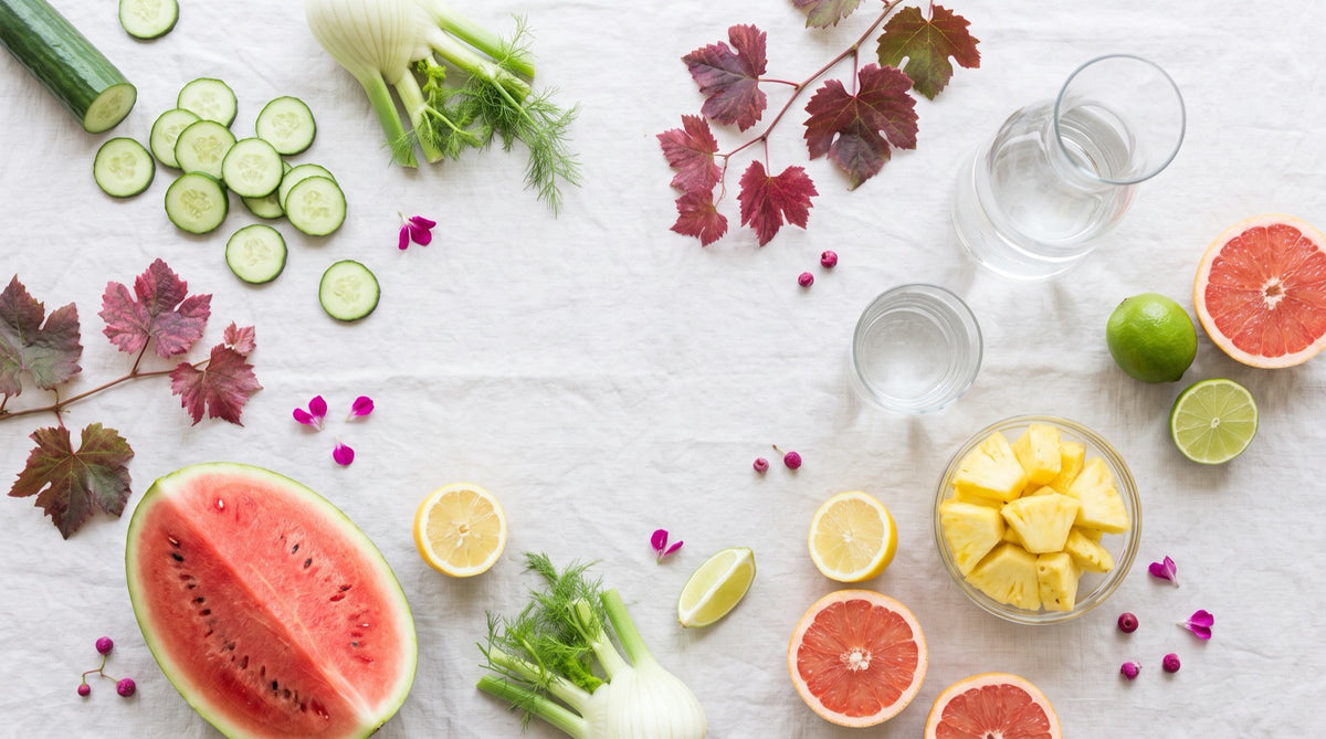 Flat lay di cibi ricchi d'acqua, cetriolo, finocchio, anguria, ananas e acqua: favorire il drenaggio delle gambe