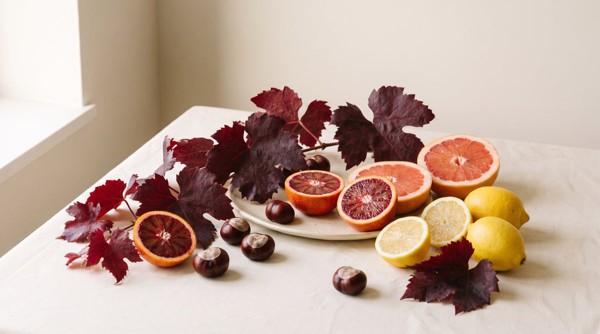 Foglie di vite rossa, agrumi e castagne su un piano di ceramica crema