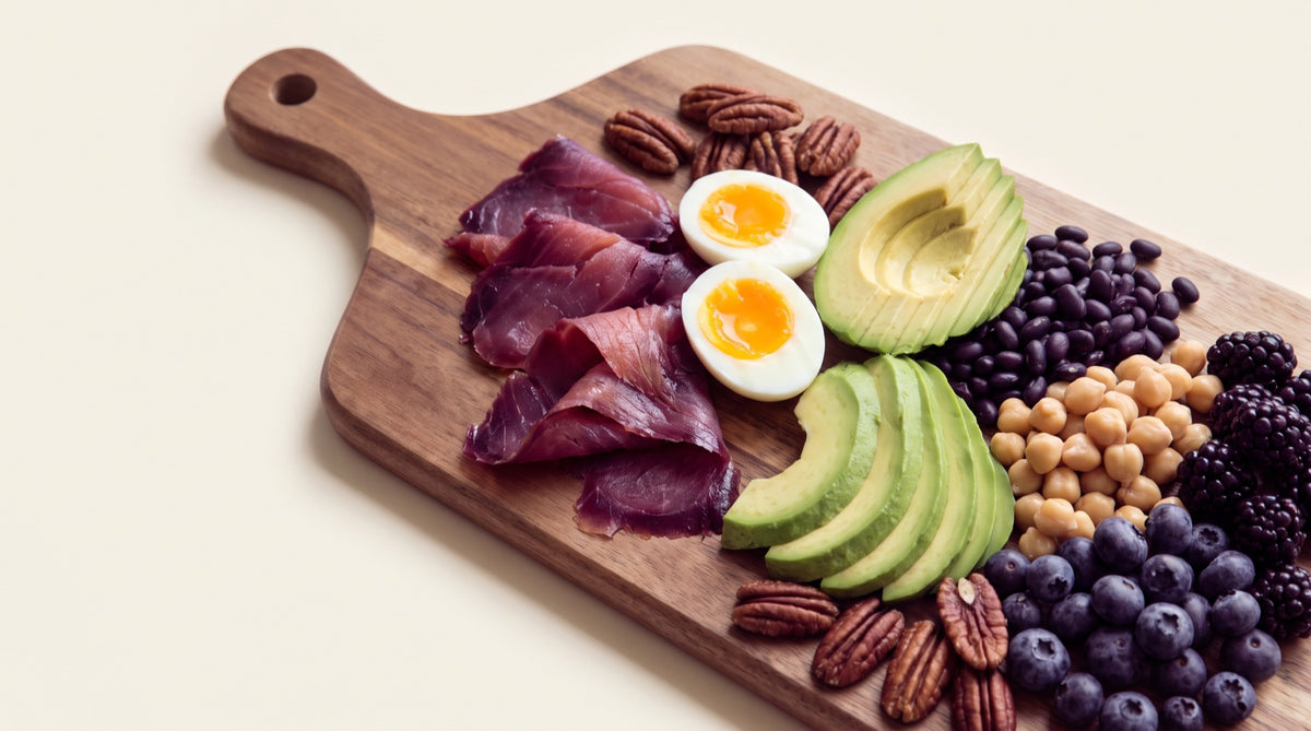 Tagliere con uova, avocado, legumi, noci e frutti di bosco